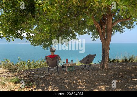 Nha Trang City, Vietnam - 30 mars 2024 : femme se reposant à l'ombre d'un arbre regardant vers la mer. Concept de relaxation Banque D'Images