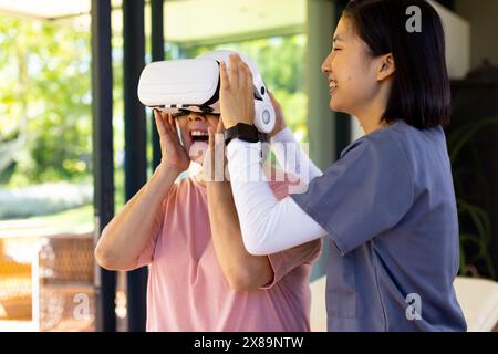 L'infirmière asiatique et le patient d'âge moyen portent des casques VR à la maison, tous deux souriants Banque D'Images