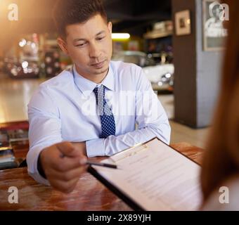 Homme, contrat et parler au client dans la concession automobile, prêt et financement pour le véhicule classique dans l'atelier. Vendeur, documentation ou paperasse pour remise Banque D'Images