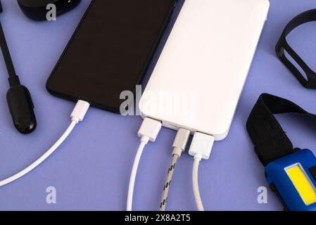 Smartphone et gadgets se chargeant avec la banque d'alimentation sur fond violet. Un ensemble de différents gadgets : une lampe de poche, une horloge électronique et un téléphone Banque D'Images