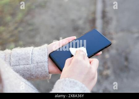 Nettoyage du téléphone portable pour éliminer les germes, coronavirus COVID-19. Photo recadrée d'une femme méconnaissable nettoyant l'écran de son appareil. Banque D'Images