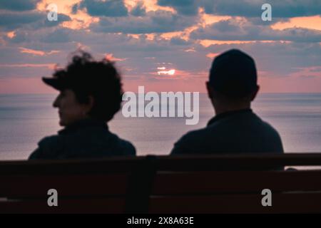 Un couple âgé est assis sur un banc, admirant les teintes pêche du coucher de soleil sur la mer Méditerranée à Dingli, Malte Banque D'Images