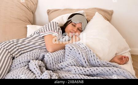 Femme en pyjama rayé gris dormant paisiblement dans le lit portant un masque pour les yeux. Banque D'Images