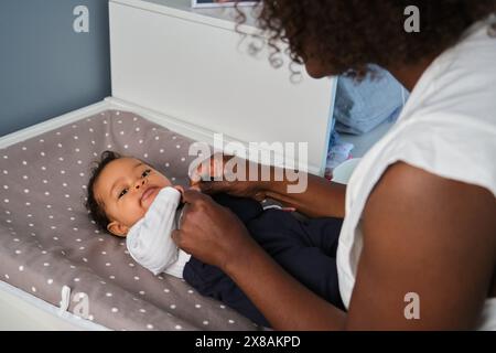 Une mère africaine habille sa petite fille sur une table à langer. Banque D'Images