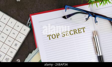 La phrase, Top secret, écrite sur la page ouverte du carnet d'affaires à côté des lunettes et de la calculatrice Banque D'Images