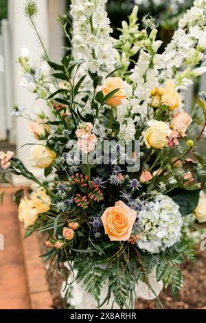 Arrangement floral avec roses pêche, fleurs blanches et verdure Banque D'Images