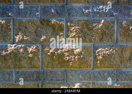 Une image en gros plan d'un mur de briques montrant sa texture rugueuse et sa couleur brune, avec la lumière du soleil projetant des ombres sur la surface, soulignant le motif Banque D'Images