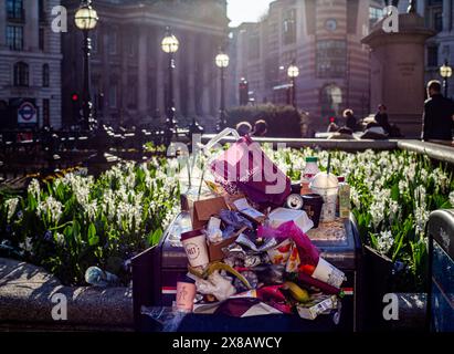 Une poubelle débordante au cœur de la City de Londres. Boites de boisson, tasses à café, bouteilles en plastique, cartons et ordures générales. Drame fort contre-jour Banque D'Images