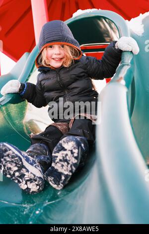 Enfant heureux jouant sur toboggan dans le terrain de jeux enneigé Banque D'Images