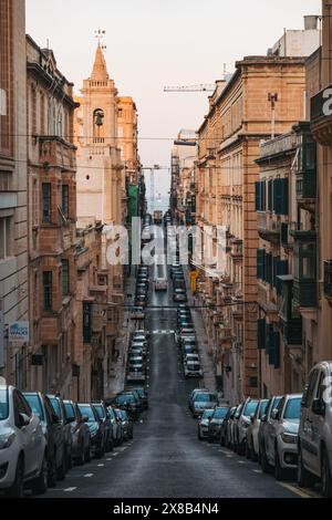 Une vue en bas d'une rue étroite avec une pente à la Valette, Malte, bordée de voitures garées des deux côtés Banque D'Images