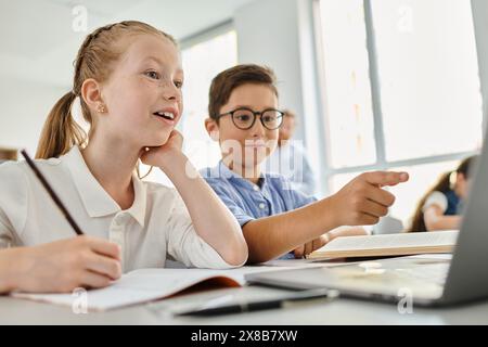 enfants assis à une table dans une salle de classe lumineuse, concentrés sur un écran d'ordinateur portable Banque D'Images