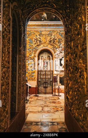 Une vue à travers une arche dorée menant à une chapelle à l'intérieur d'une cathédrale de Malte, révélant des sculptures complexes et des détails ornés. Banque D'Images