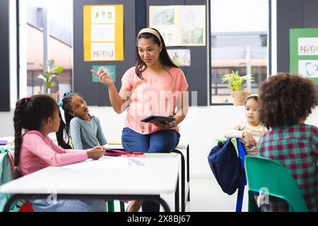 À l'école, en classe, une jeune enseignante biraciale explique à ses élèves divers Banque D'Images