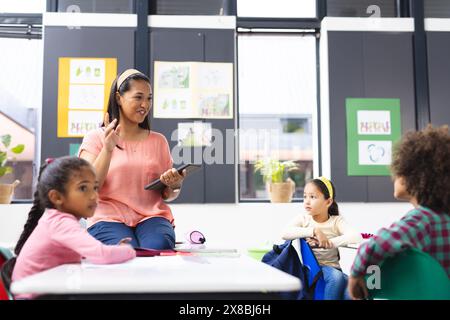 À l'école, en classe, famille diversifiée avec une jeune mère enseignant ses jeunes enfants Banque D'Images