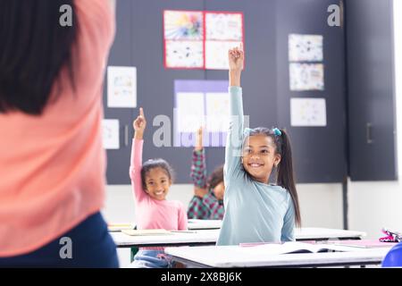 À l'école, une jeune enseignante biraciale se tient face à sa classe diversifiée dans la salle de classe Banque D'Images