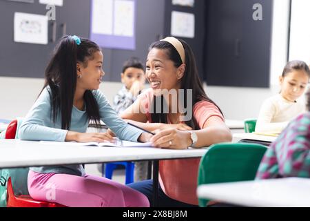 À l'école, une jeune enseignante biraciale parle à une jeune fille biraciale dans la salle de classe Banque D'Images