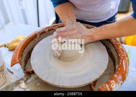 Un artiste fait des plats en argile en utilisant les mains mouillées sur la roue de potier Banque D'Images