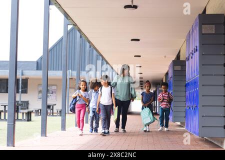 À l'école, groupe diversifié d'élèves marchant avec leur professeur à l'extérieur Banque D'Images