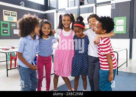 À l'école, un groupe diversifié de jeunes étudiants s'étreignent et rient ensemble dans la salle de classe Banque D'Images