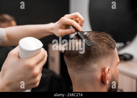 Un barbier pulvérise et peigne les cheveux des hommes au salon de coiffure. Banque D'Images