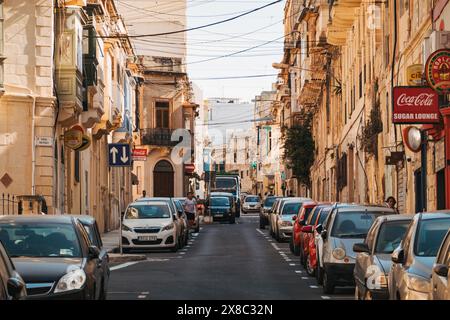 Véhicules compacts garés le long d'une rue résidentielle étroite bordée de bâtiments calcaires dans la ville de Sliema, Malte, par un après-midi ensoleillé Banque D'Images