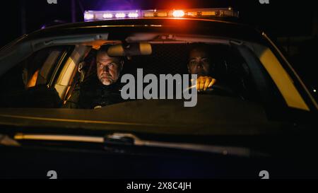 Point de vue : quart de nuit deux policiers en service conduisant une voiture de patrouille de la circulation, allumez les lampes de poche de sirène et commencez à chasser un suspect. Escouade des flics de voiture à la poursuite du criminel. Prise de vue nocturne cinématographique Banque D'Images