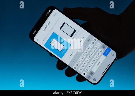 New York, États-Unis - 6 mai 2024 : création d'une application mobile sur smartphone dans la main isolé fond bleu dégradé Banque D'Images