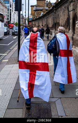 Un couple d'âge moyen enveloppé dans Cross of St George Flags marche vers la gare routière de Victoria après les célébrations de la St George's Day à Londres, au Royaume-Uni. Banque D'Images