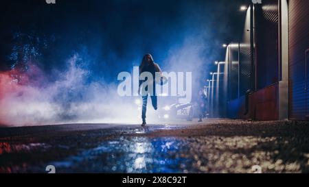 Deux policiers courent après un suspect. Des officiers héroïques de la loi essaient d'attraper et d'arrêter dangereux criminel sur la rue Dark City. Les flics arrêtent un criminel, combattent le crime. Cinématographique Banque D'Images