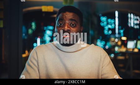 POV de caméra avec un chef de projet afro-américain multiethnique excité effectuant un appel vidéo du bureau dans la soirée. Spécialiste masculin parlant à un collègue par le biais d'une caméra en direct. Banque D'Images