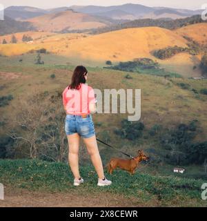 Femme brésilienne se promène avec son chien à la campagne de Santa Branca, Brésil pendant le coucher du soleil. Banque D'Images