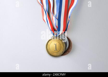 Groupe de médailles d'or en argent et en bronze empilées les unes sur les autres avec un ruban bleu blanc et rouge sur fond blanc. Vue de dessus. Banque D'Images