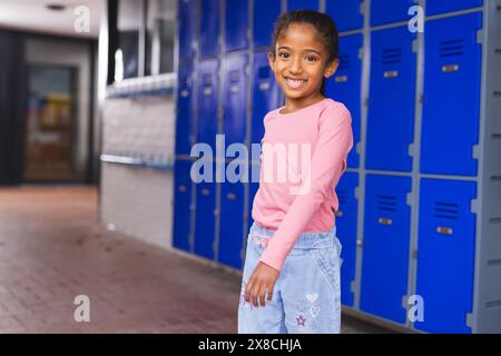 À l'école, la jeune fille biraciale se tient près de casiers bleus avec espace de copie Banque D'Images