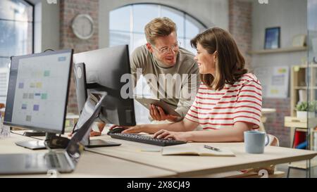 Portrait de deux collègues créatifs utilisant un ordinateur et une tablette pour discuter du projet de travail. Jeune spécialiste du support technique caucasien aidant la coordonnatrice des relations avec la clientèle féminine. Concept de travail d'équipe Banque D'Images