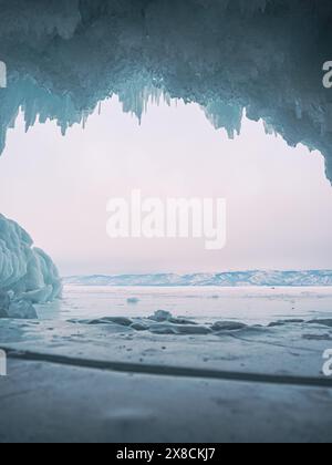 À l'intérieur d'une magnifique grotte de glace sur le lac Baïkal, de grands glaçons pendent du plafond, créant un paysage hivernal à couper le souffle. Les montagnes enneigées peuvent Banque D'Images