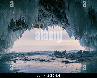 À l'intérieur d'une magnifique grotte de glace sur le lac Baïkal, de grands glaçons pendent du plafond, créant un paysage hivernal à couper le souffle. Les montagnes enneigées peuvent Banque D'Images