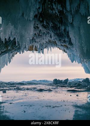 À l'intérieur d'une magnifique grotte de glace sur le lac Baïkal, de grands glaçons pendent du plafond, créant un paysage hivernal à couper le souffle. Les montagnes enneigées peuvent Banque D'Images