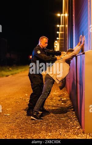 Un policier professionnel d'âge moyen effectuant une recherche Pat-Down sur un Fellon dans Empty Back Alley. Plan documentaire de la procédure appropriée d'arrestation des suspects. Policier expérimenté à la recherche d'armes Banque D'Images