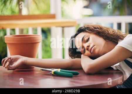 Outil de jardin, femme endormie et fatiguée dans la pépinière de plantes sur la table pour le démarrage de l'agro-industrie. Épuisé, jardinage et aménagement paysager avec jeune fleuriste Banque D'Images