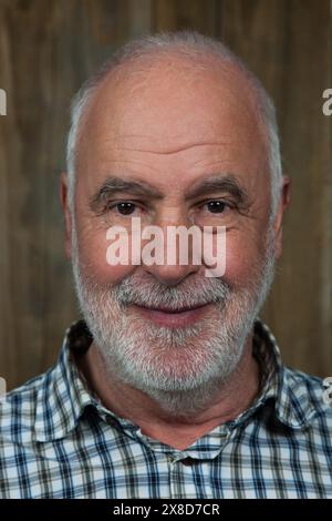 Un homme plus âgé aux cheveux gris et à la barbe grise sourit chaleureusement à la caméra. Banque D'Images