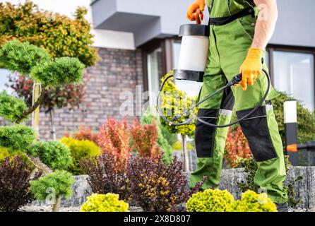 Jardinier caucasien en combinaison de protection pulvérisant des pesticides sur l'arbre et d'autres plantes à l'intérieur d'un jardin. Banque D'Images