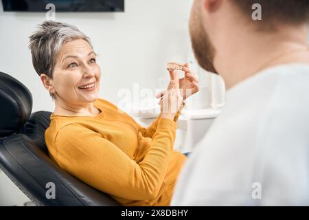 Femme surprise tenant dans les mains le modèle 3d de ses dents supérieures Banque D'Images