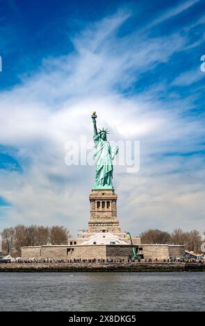 Lady Liberty illumine le chemin ! Capturez le symbole emblématique de la liberté, sa torche tenue haute contre un ciel bleu clair. Idéal pour le contenu de voyage et d'histoire. Banque D'Images