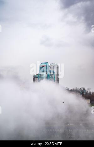 Côté canadien des chutes du Niagara enveloppé dans la brume. Les bâtiments imposants jettent un œil à travers les nuages, créant un air de mystère. Idéal pour le paysage de voyage. Banque D'Images