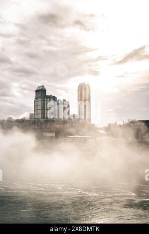 Côté canadien des chutes du Niagara enveloppé dans la brume. Les bâtiments imposants jettent un œil à travers les nuages, créant un air de mystère. Idéal pour le paysage de voyage. Banque D'Images