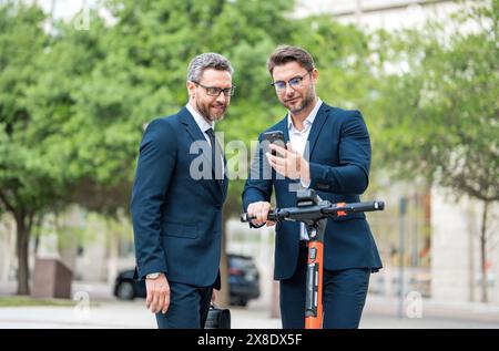 Hommes d'affaires utilisant le téléphone portable en plein air. Homme d'affaires mature confiant parlant sur le téléphone portable tout en marchant à l'extérieur. Hommes d'affaires regardant les messages Banque D'Images