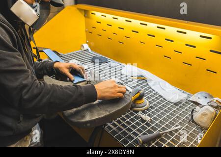 technicien avec masque polissant la guitare électrique moderne en fibre de carbone dans l'atelier. Photo de haute qualité Banque D'Images