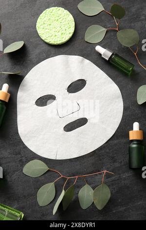 Masque de drap facial avec différents produits cosmétiques et eucalyptus sur fond noir Banque D'Images