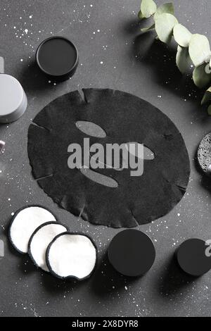 Masque de drap facial avec différents produits cosmétiques et eucalyptus sur fond noir Banque D'Images