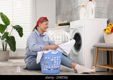 Heureuse femme au foyer mettant le linge dans la machine à laver à la maison Banque D'Images